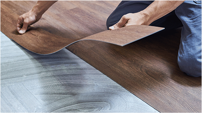 Person placing vinyl plank flooring over an underlayer in a modern interior.