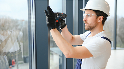 A worker wearing a helmet is installing a modern window using a power drill.