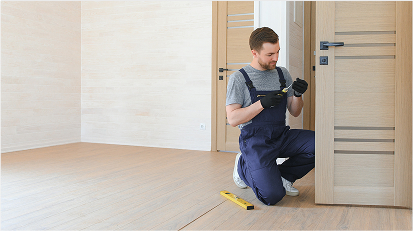 A man is installing an interior door in a room with a wooden floor.