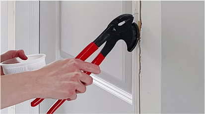 Someone is removing old trim from a doorframe using pliers.