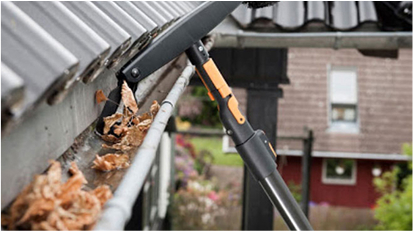 A person cleaning leaves from gutters on a roof using a tool.