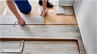 Two people installing or fixing wooden floorboards indoors.