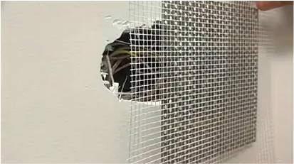 A close-up of a wall with a hole covered by a mesh, showing drywall repair in progress.