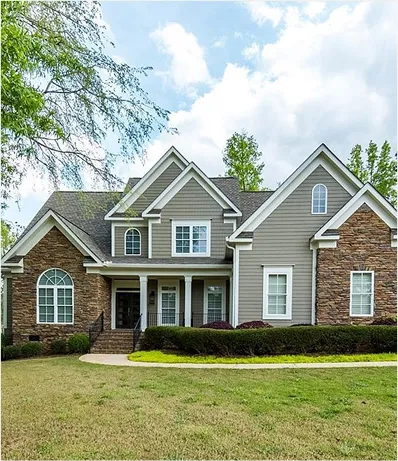Modern two-story suburban house with a combination of gray siding and stone facade, featuring multiple gables, white-trimmed windows, a front porch, and a well-maintained lawn.