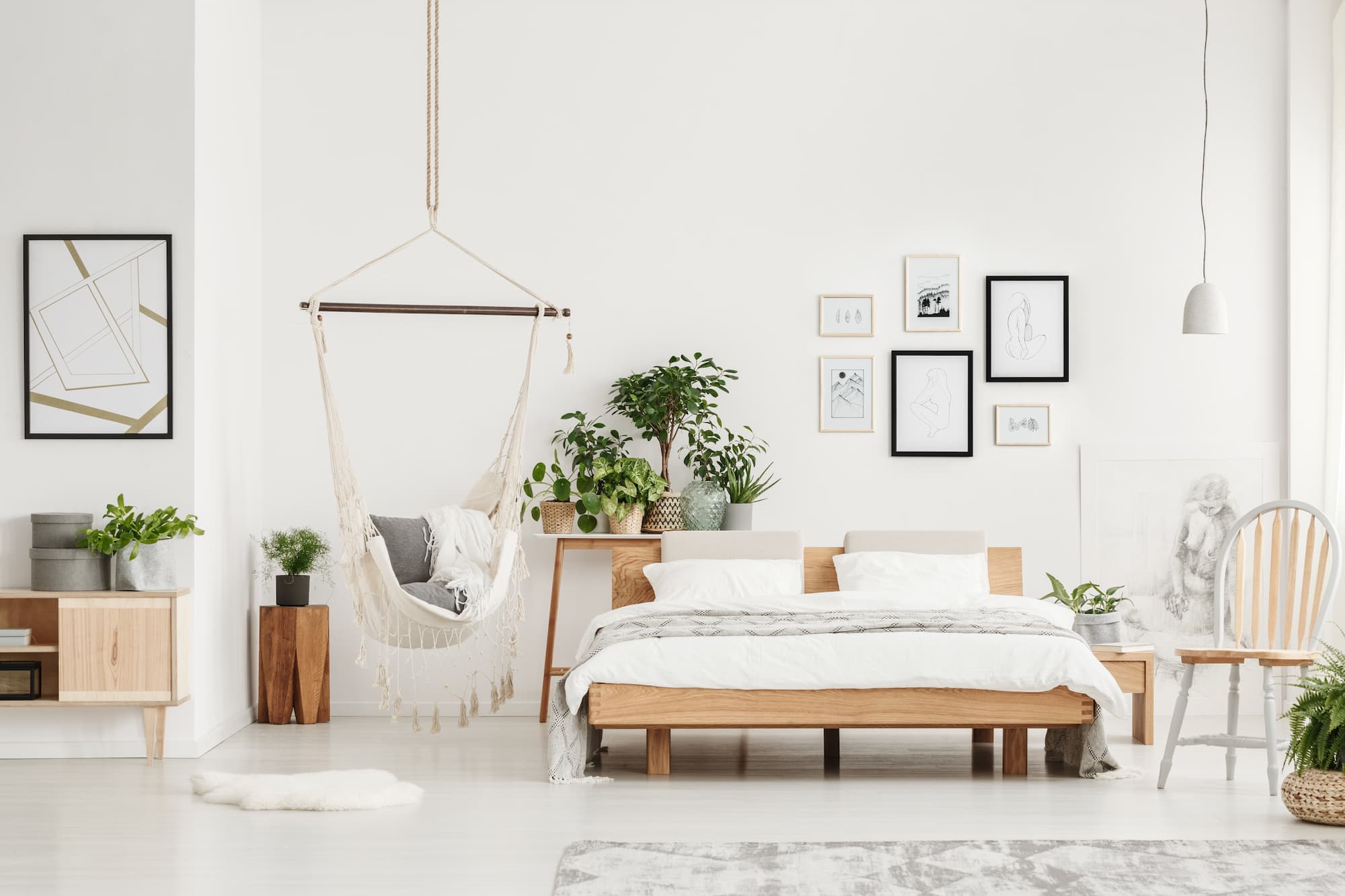 Contemporary bedroom styled with indoor plants, natural wood bed and a hanging hammock chair for a relaxed, nature-inspired interior