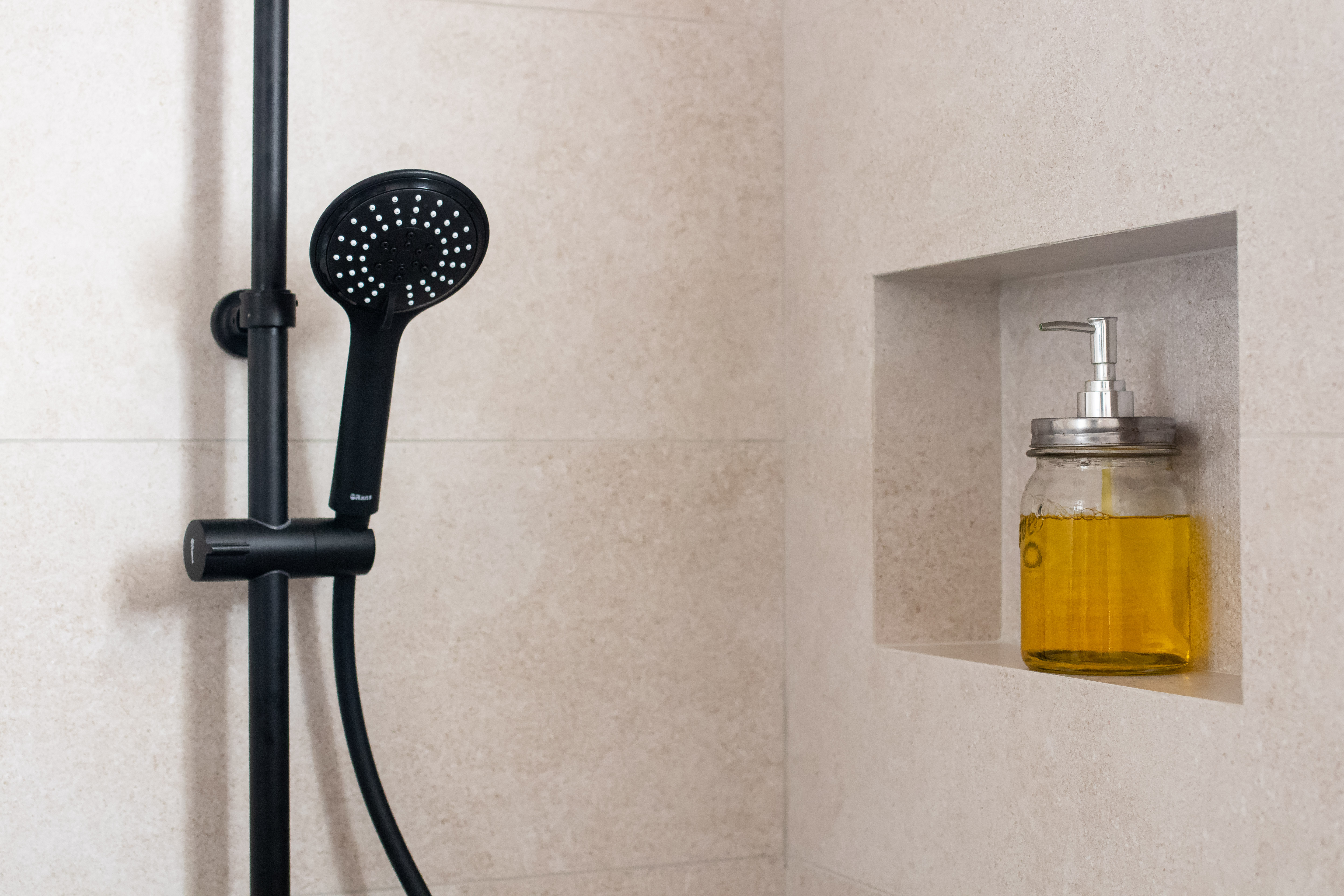 Detail of matte black rainfall shower in a contemporary bathroom design with natural stone-effect tiles.