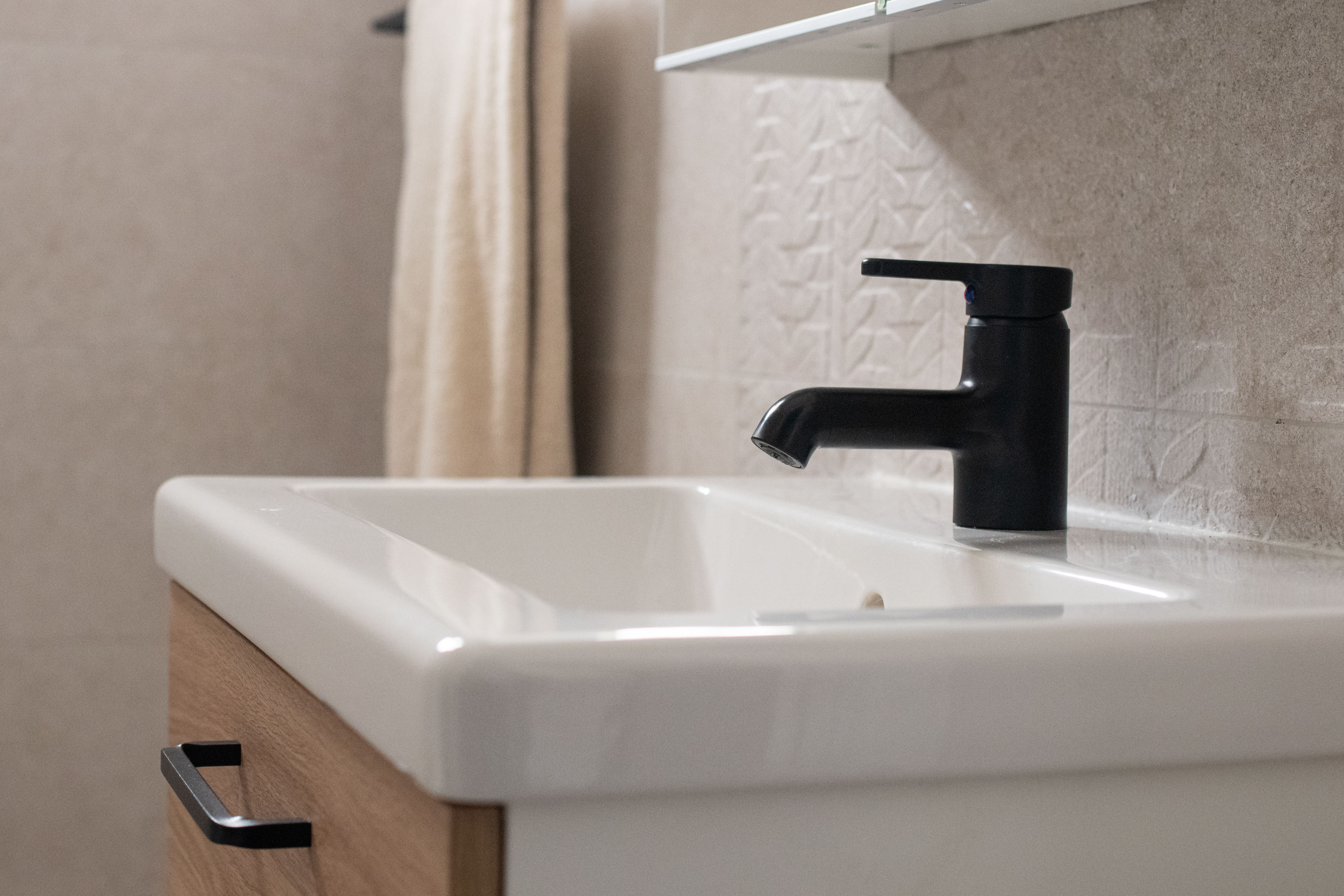 Modern bathroom basin with black tap and oak-effect vanity unit, ideal for small-space renovations.