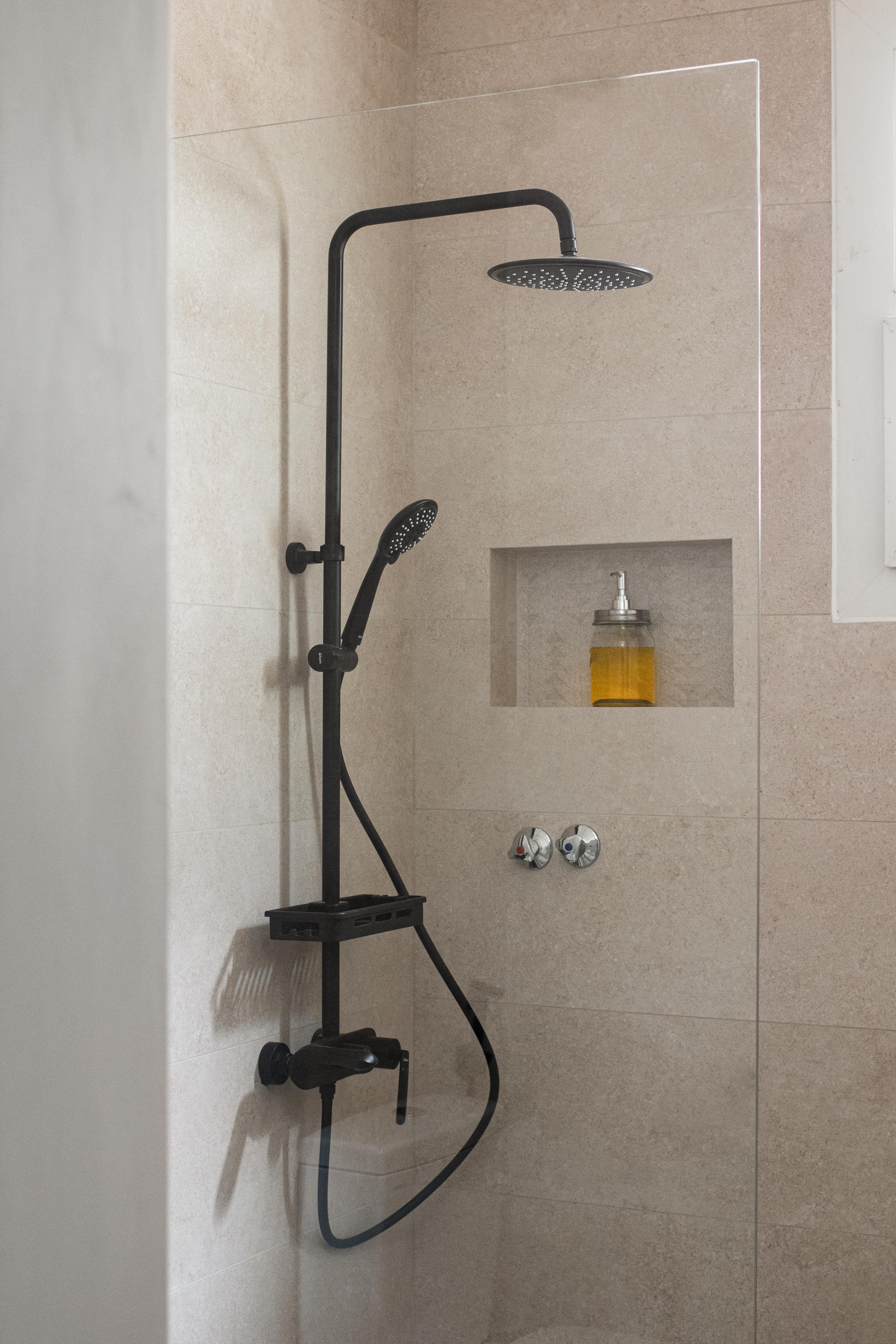 Stylish walk in shower design with built in niche, soft stone effect tiles, and black rainfall fittings. Ideal for property renovations in Leeds.