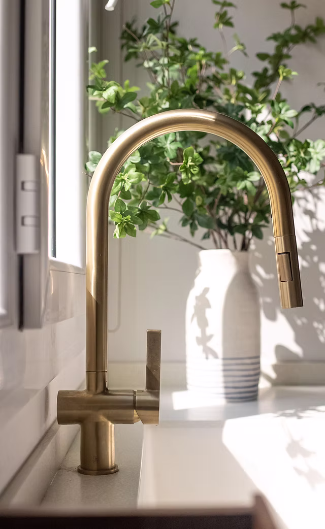 Minimalist gold kitchen tap with ceramic vase and greenery – modern kitchen detail from a Roberts Renovations design.
