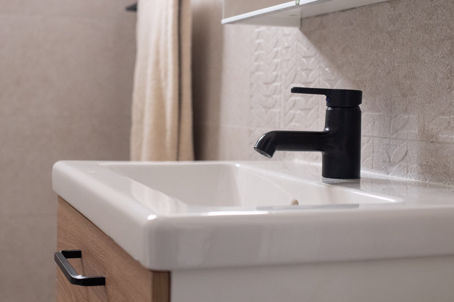 Modern bathroom sink with black tap, neutral-toned tiles, and recessed mirror creating a sleek and elegant design.