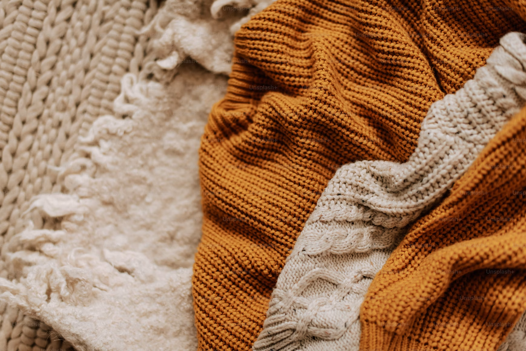 Chunky knit throw and faux fur blanket draped over a sofa in earthy tones of green and cream, styled for cosy winter home décor and 2025 interior design trends.