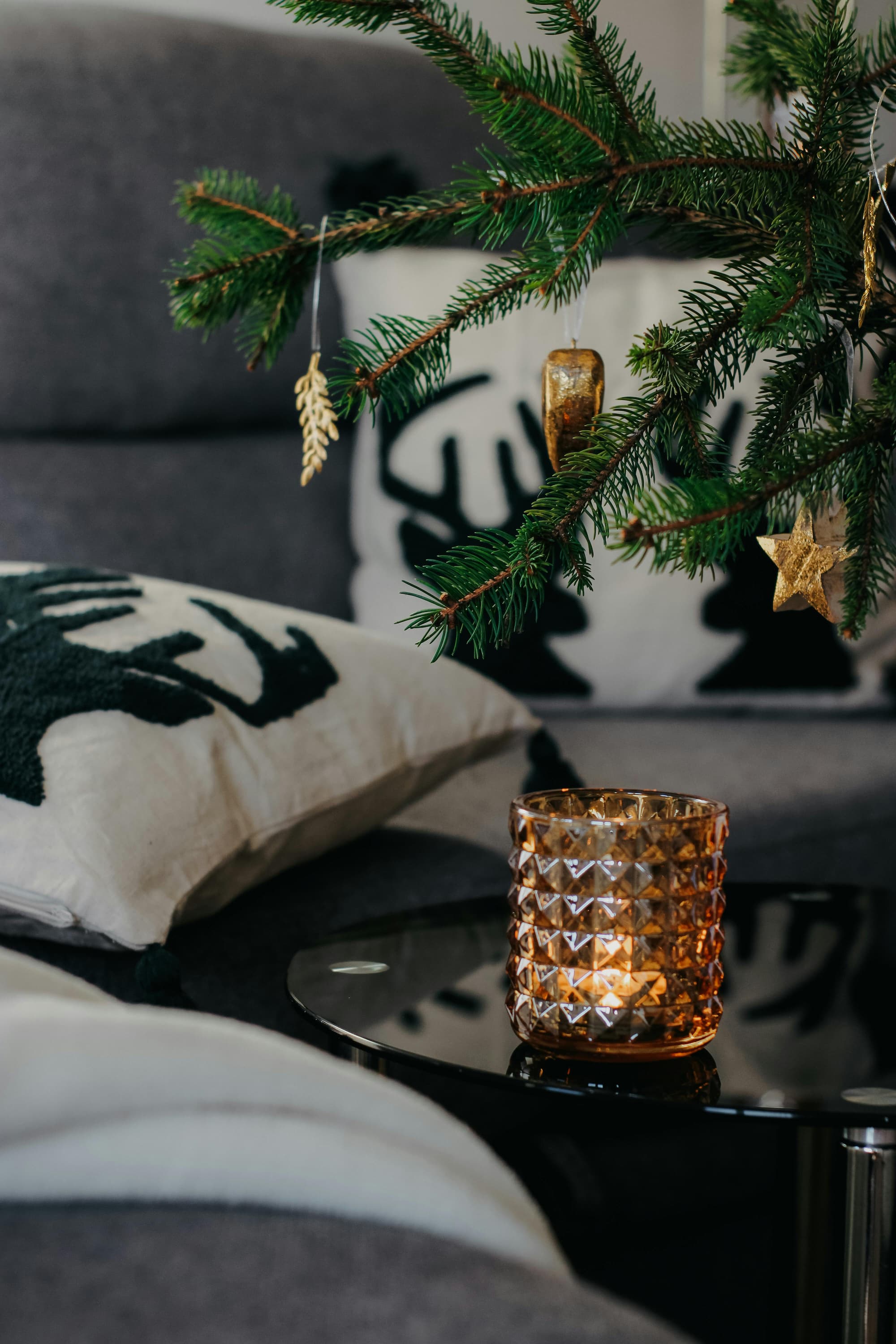 Cushions with winter-inspired patterns on a grey sofa beside a glowing candle, showing cosy home styling and 2025 winter interior design trends.