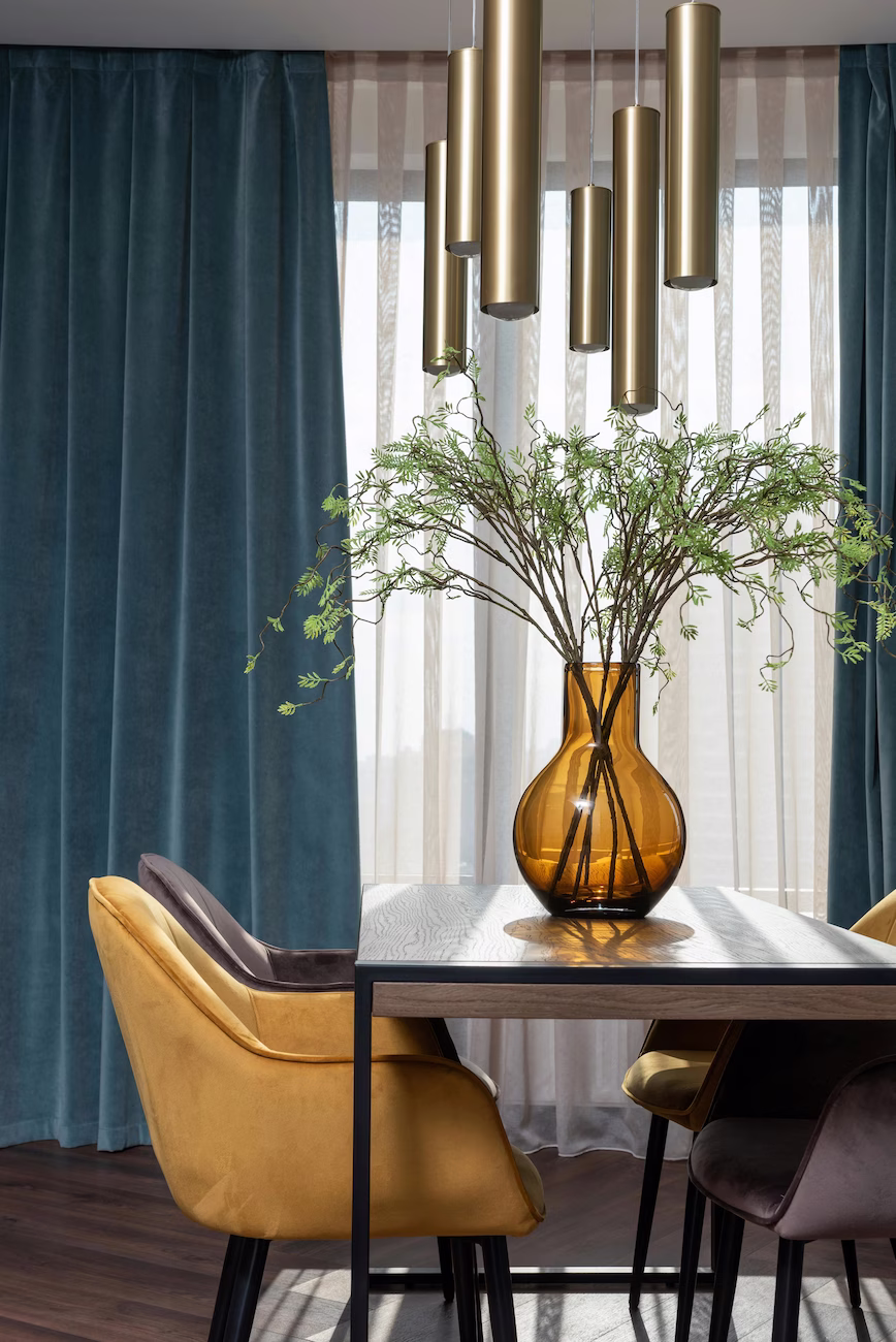 Modern dining room interior designed by Roberts Renovations, featuring gold pendant lighting, blue velvet curtains, and mustard upholstered chairs for a bold, contemporary look.