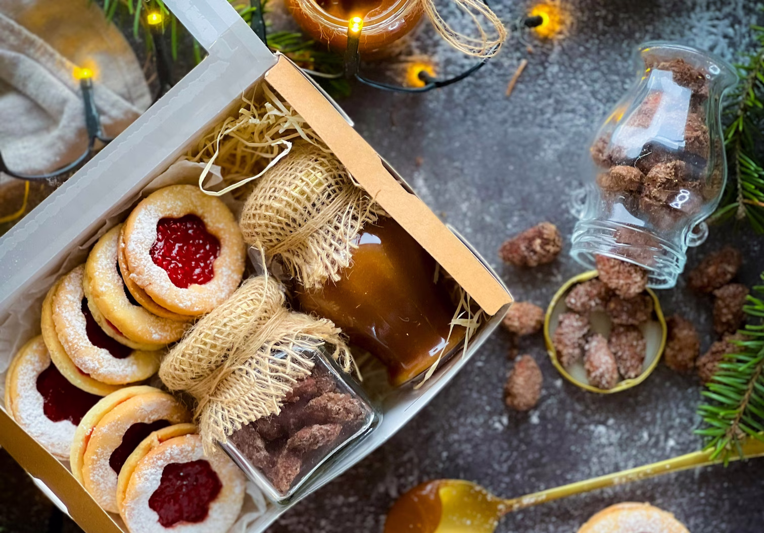 Homemade Christmas biscuits and festive treats arranged in a rustic gift box with caramel jars, sugared nuts, and warm fairy lights for cosy holiday décor inspiration.
