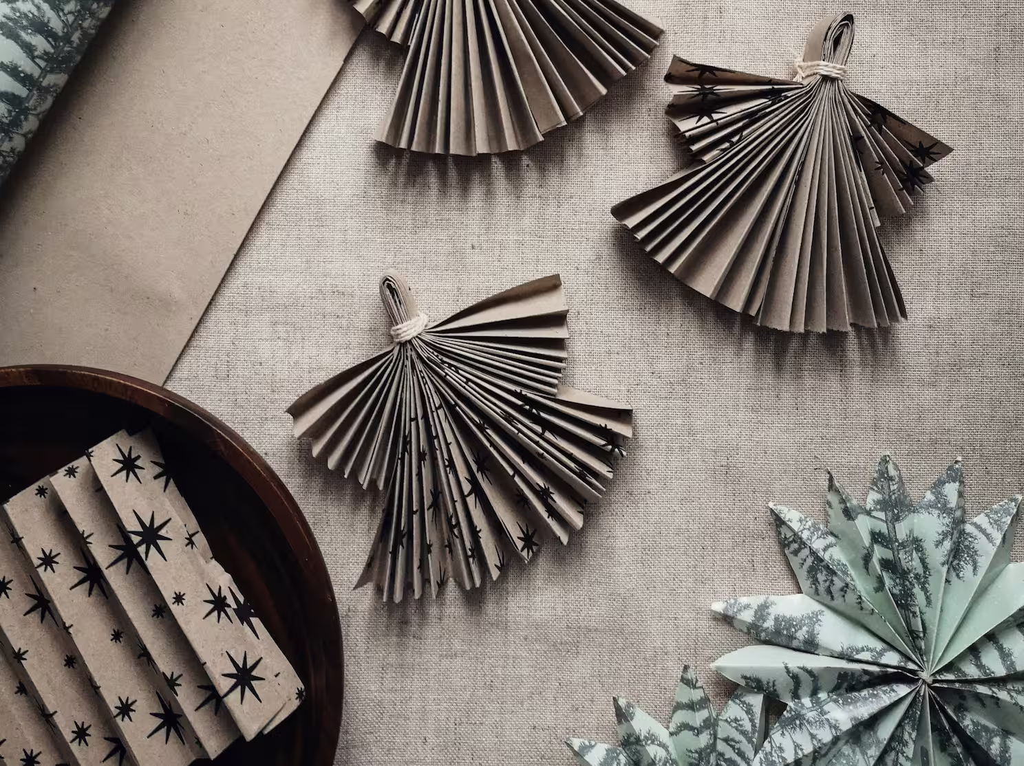 Handmade paper Christmas decorations, including folded paper angels and stars, displayed on a natural fabric surface for sustainable festive craft inspiration.