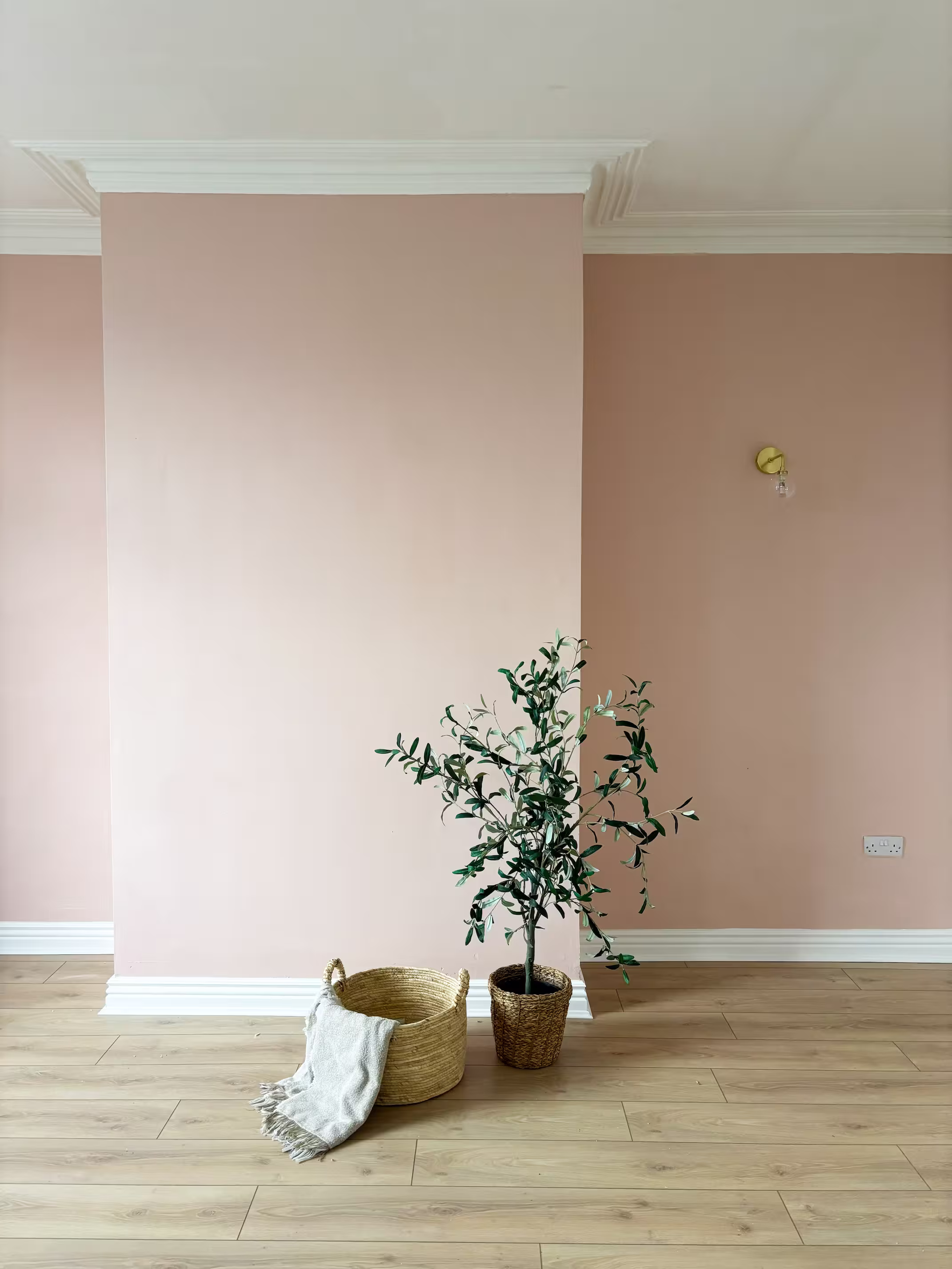 Interior detail of renovated room with blush pink feature wall, wall light and wooden laminate flooring in Pudsey property refurbishment