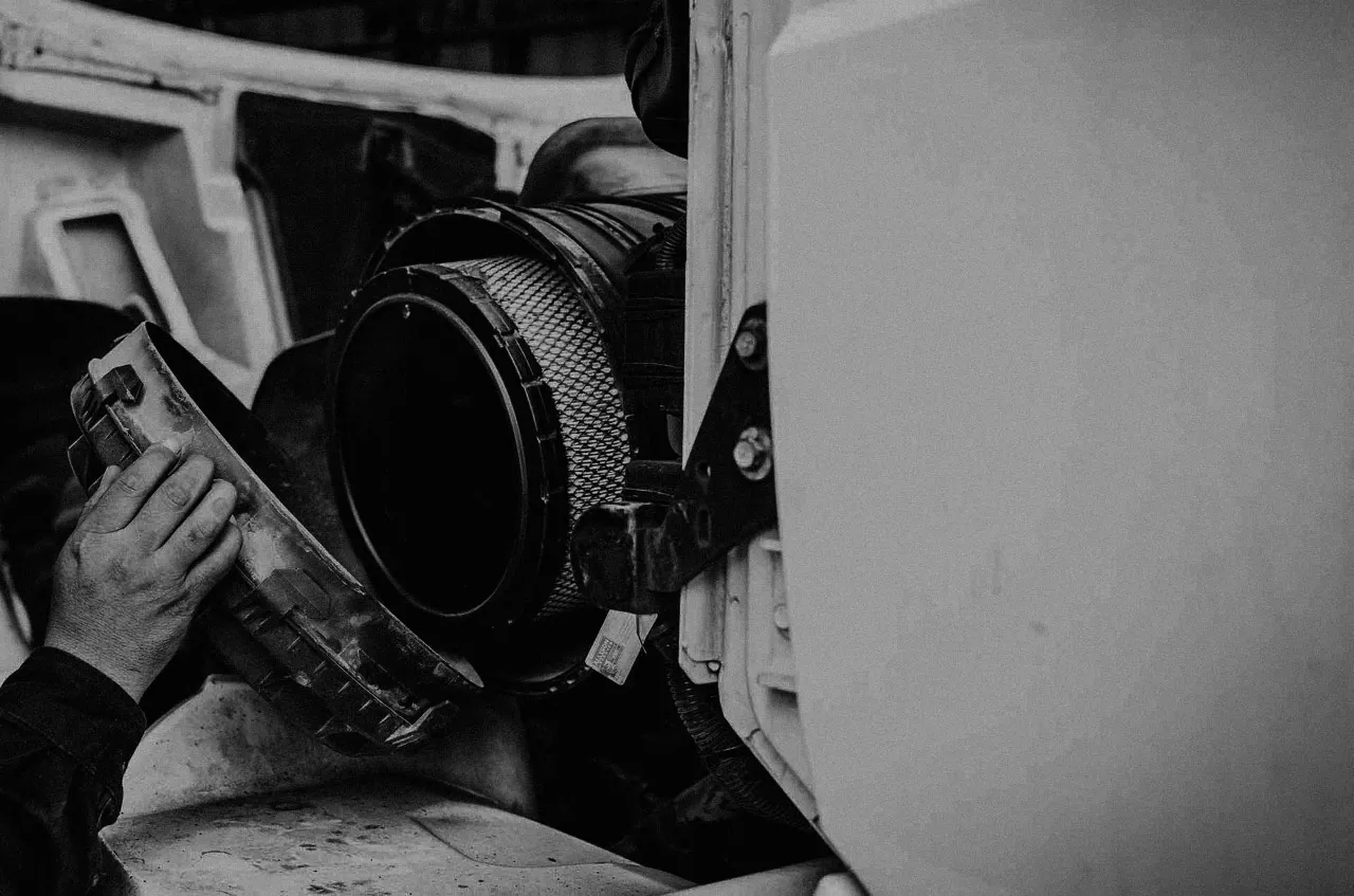 Technician removes housing to access EGR system air filter on a heavy-duty truck during maintenance.