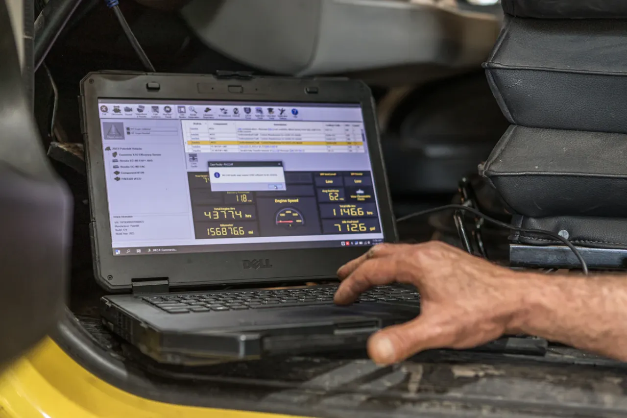 Technician using diagnostic software on a laptop to monitor engine hours and speed for preventive maintenance.
