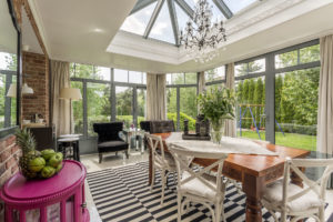 A beautifully designed sunroom with a wooden table and chandelier in the middle.