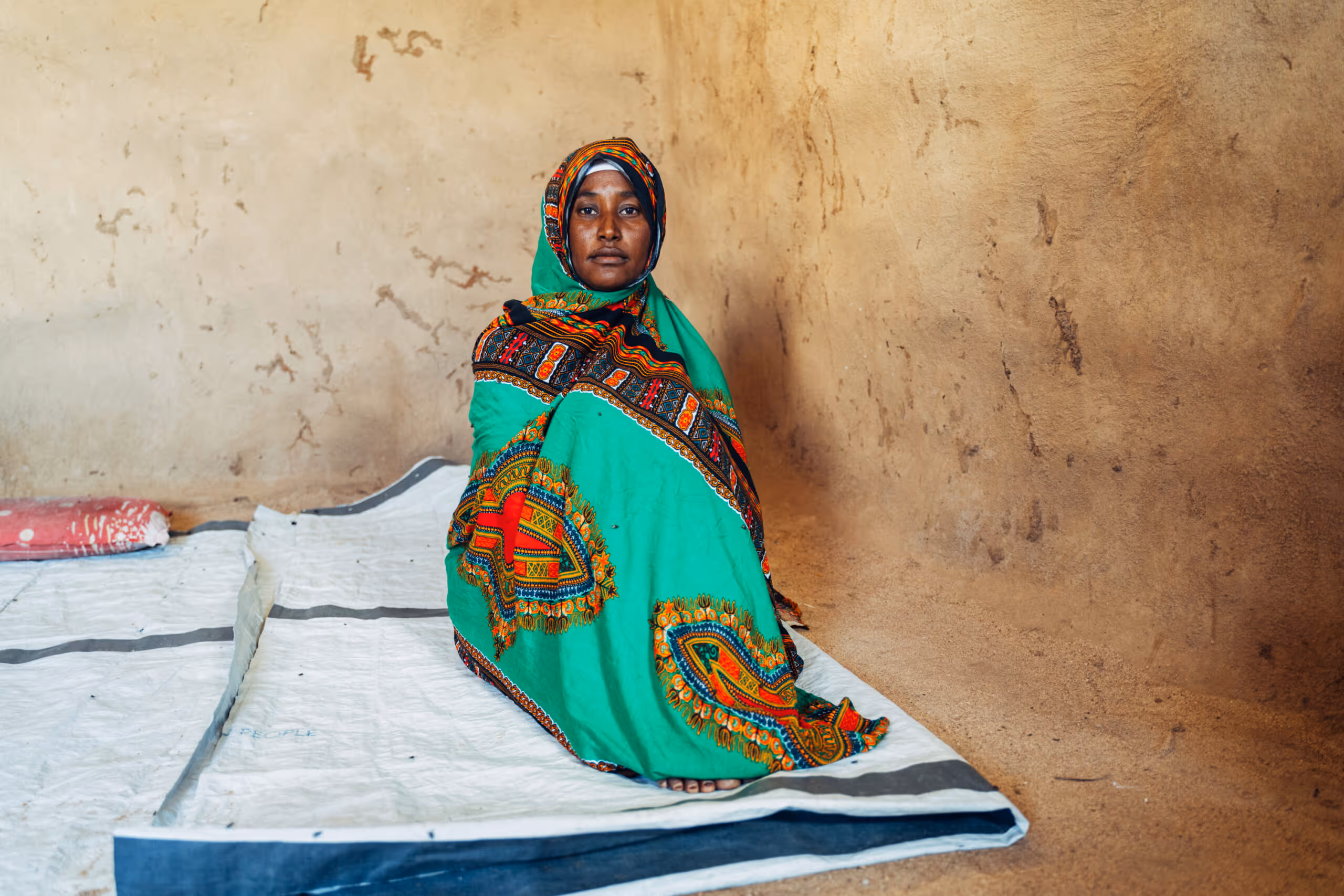 a woman sits wrapped up in fabric on a bare blanket against a blank wall