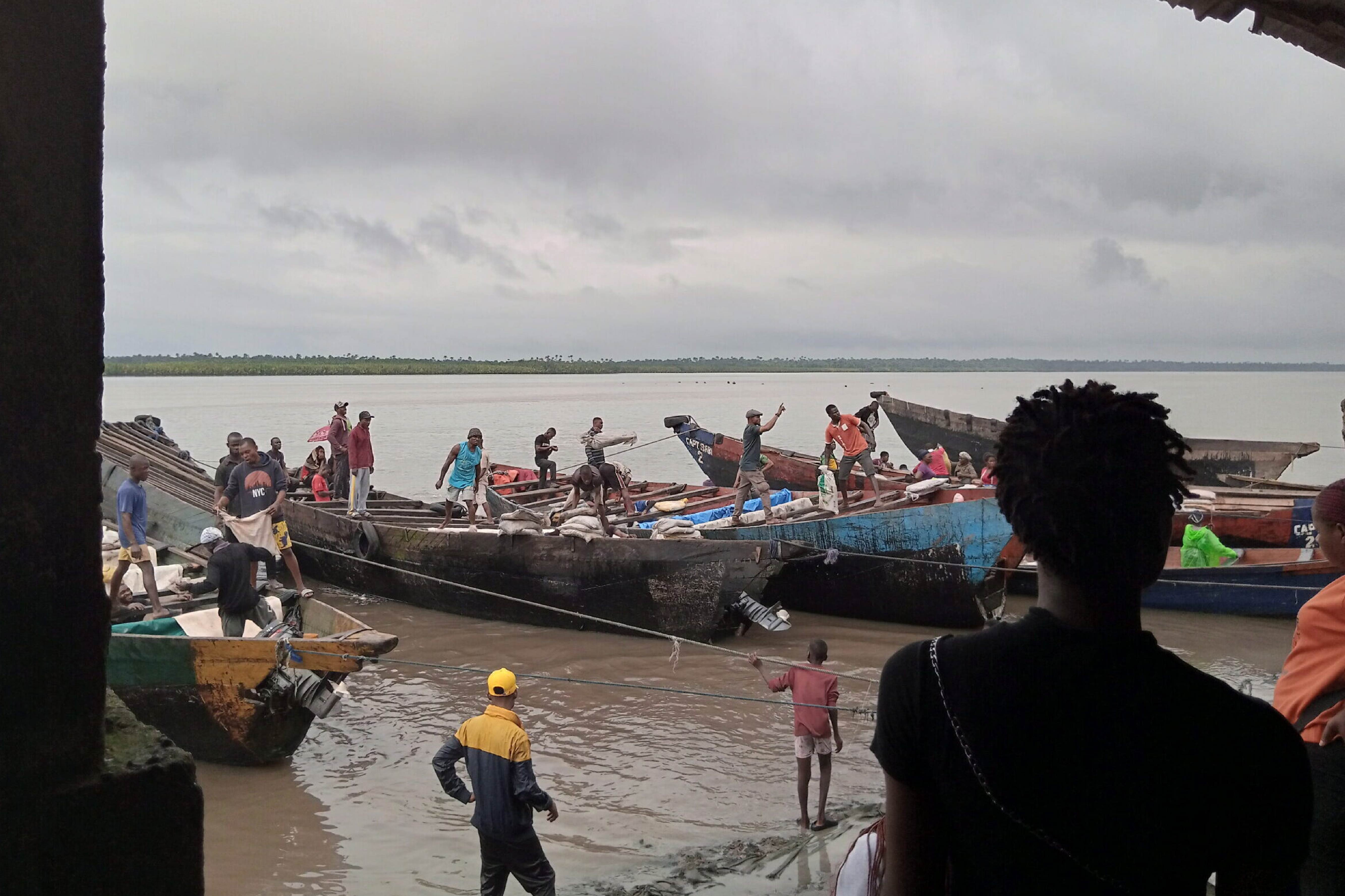 A series of boats fill with people on the shoreline with others on shore