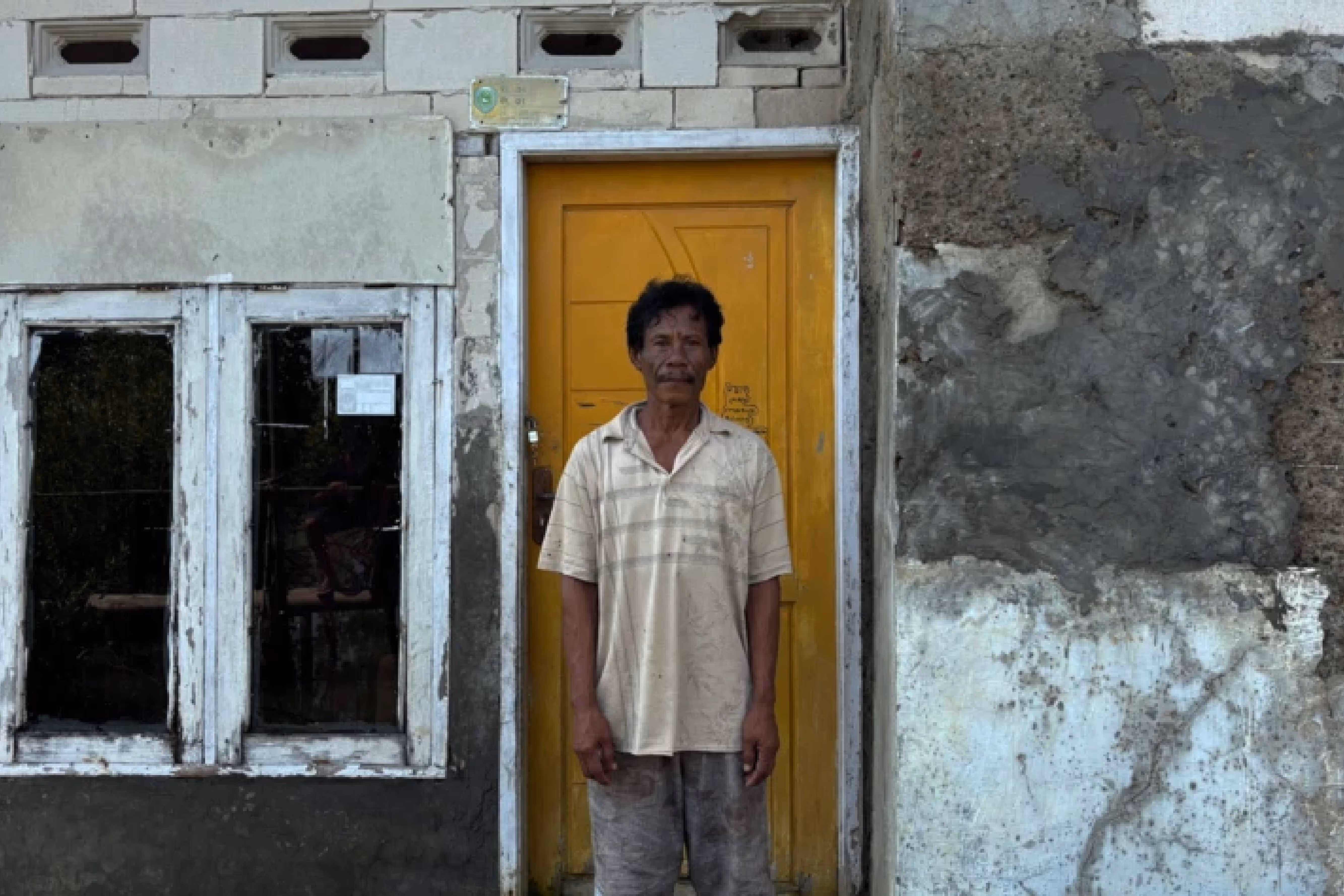 A man stands in front of a yellow door within a dilapidated building
