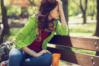 A person sitting on a park bench with their hand on their forehead, appearing stressed or tired.