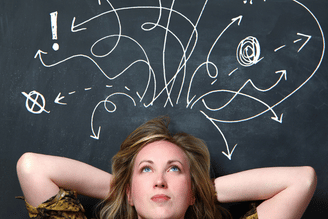 A person with hands behind their head looks up at a chalkboard covered in swirling white arrows and symbols, suggesting a complex thought process.