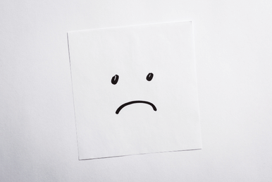 A white square paper with a sad face drawn on it in black marker.