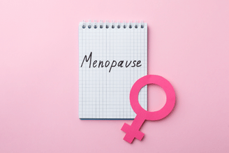A notebook with the word "Menopause" written on it, next to a pink female symbol on a pink background.