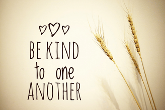 Three stalks of wheat are shown next to the words "BE KIND to one ANOTHER" written in dark lettering with three small hearts above the text.
