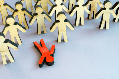 Wooden human-shaped figures scattered across a blue surface, with one red figure separated in the center and many yellow figures surrounding it.