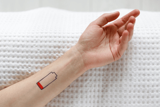  Close-up of a forearm resting on a textured white blanket, showing a rectangular tattoo-like design with red and black coloring near the wrist.