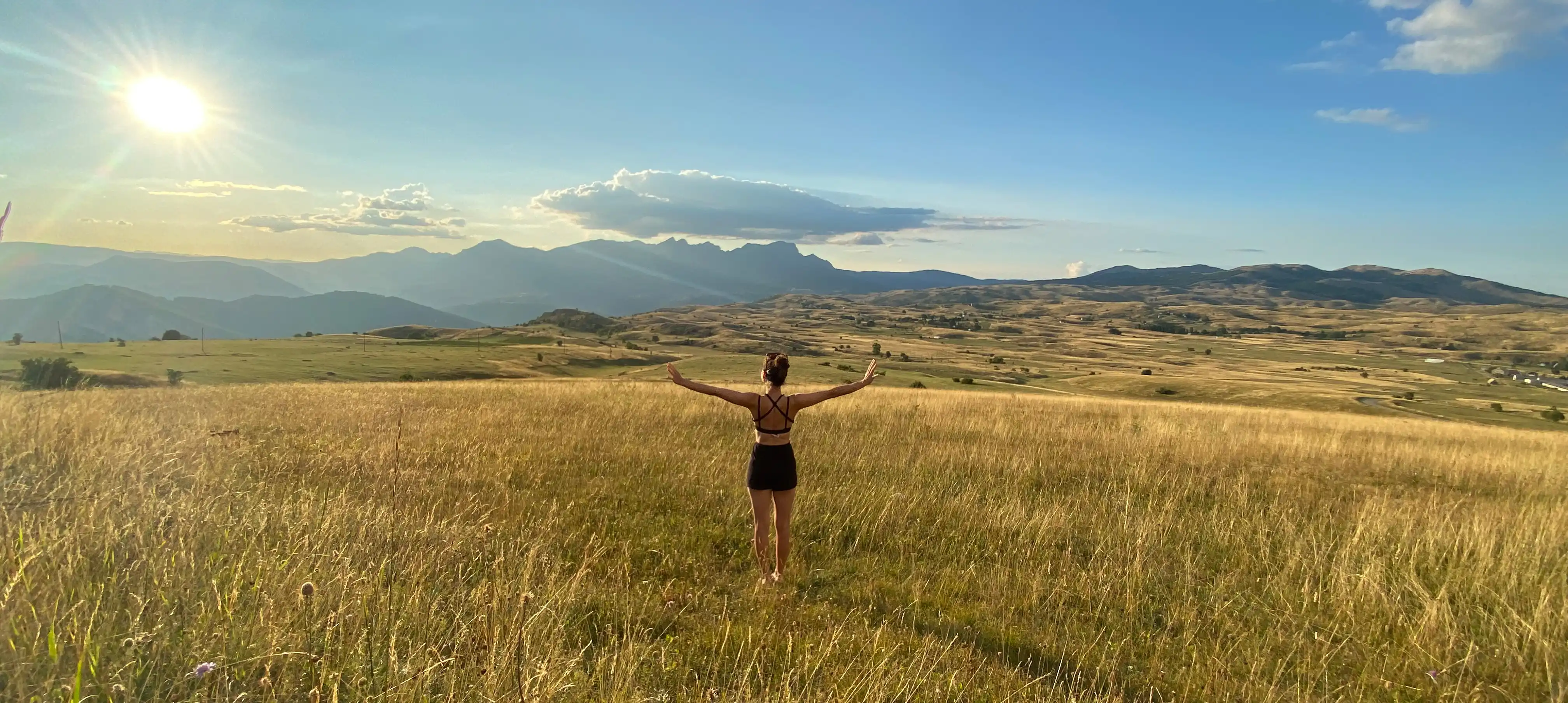 Osteopathin und Heilpraktikerin Viktoria Weinzierl auf einer Bergwiese mit Weitblick, Arme zur Seite gestreckt – Symbol für natürliche Ruhe, Gesundheit und innere Balanc