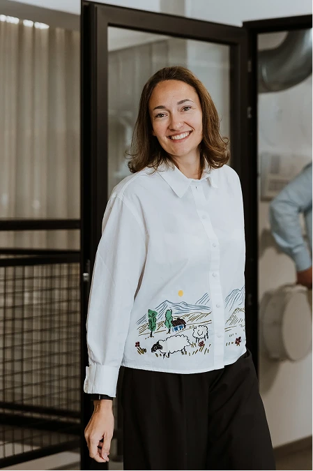 Two people working at adjacent desks in a bright modern office, separated by a concrete pillar