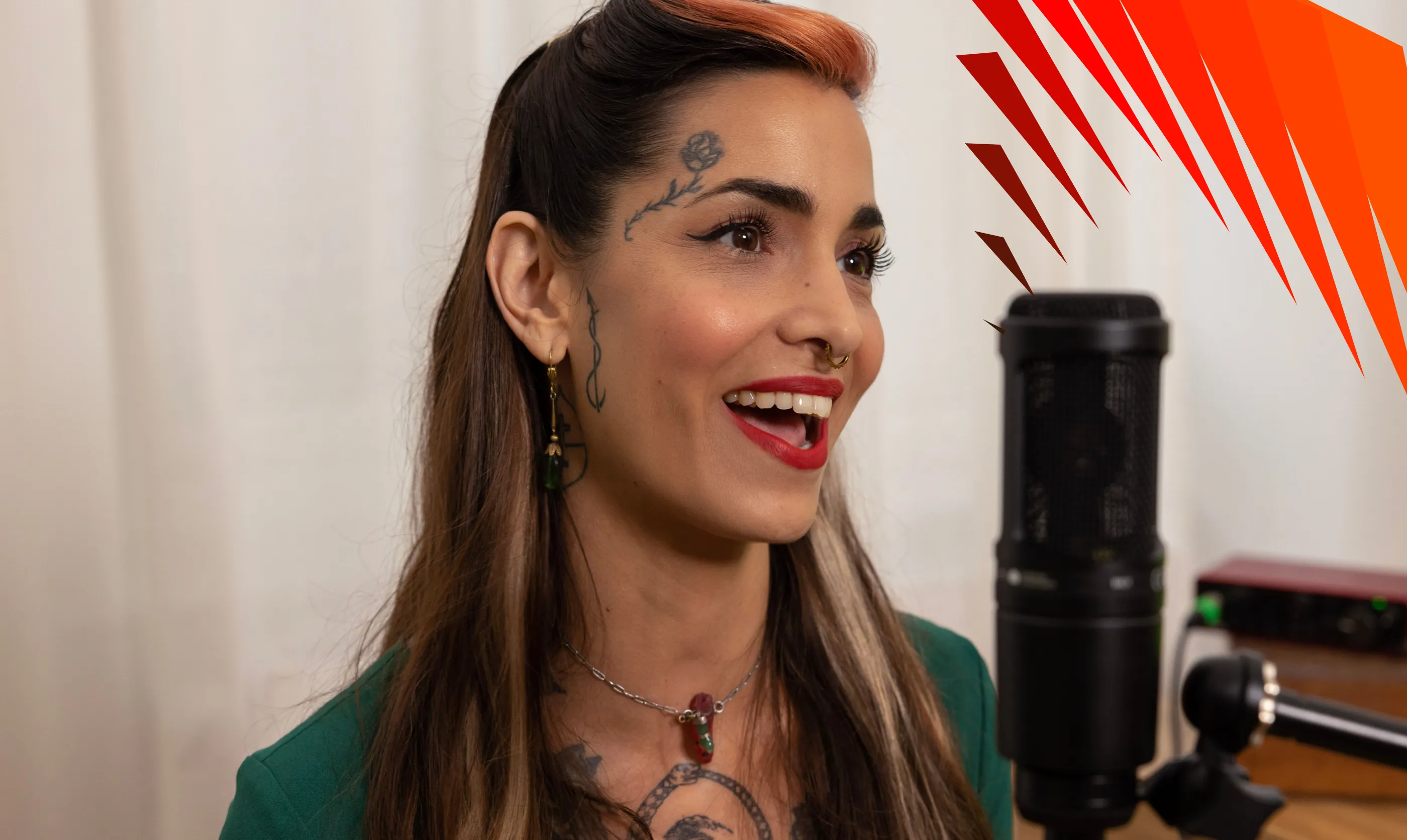 Woman with face tattoos and red lipstick singing into a studio microphone.