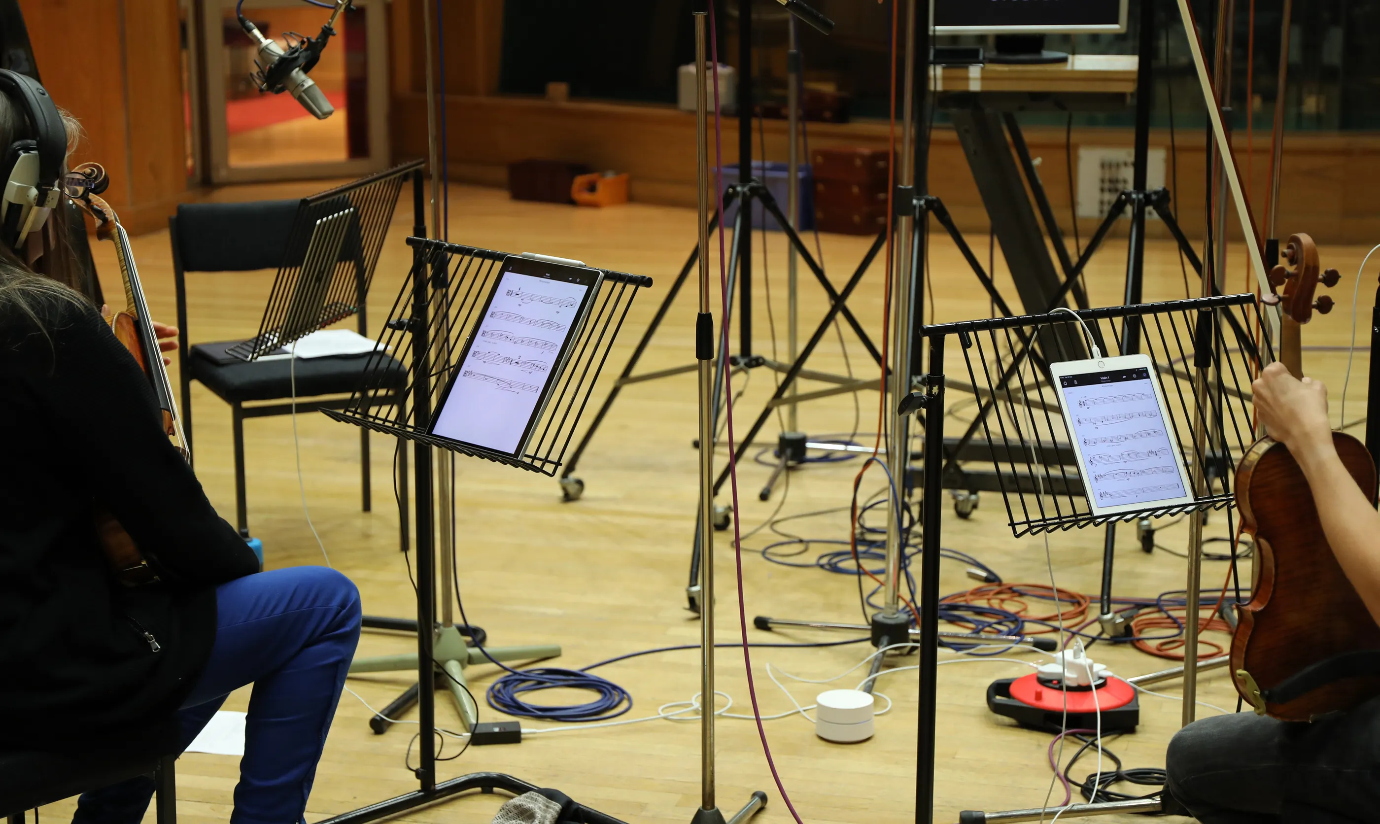 A woman playing a cream-colored electric guitar while sitting on a couch, photographed from above, with vibrant pink and yellow graphic streaks overlaying the right side of the image.