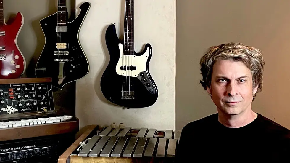Composer Josh Mancell sitting in a music studio with guitars, a synthesizer, and a vibraphone in the background