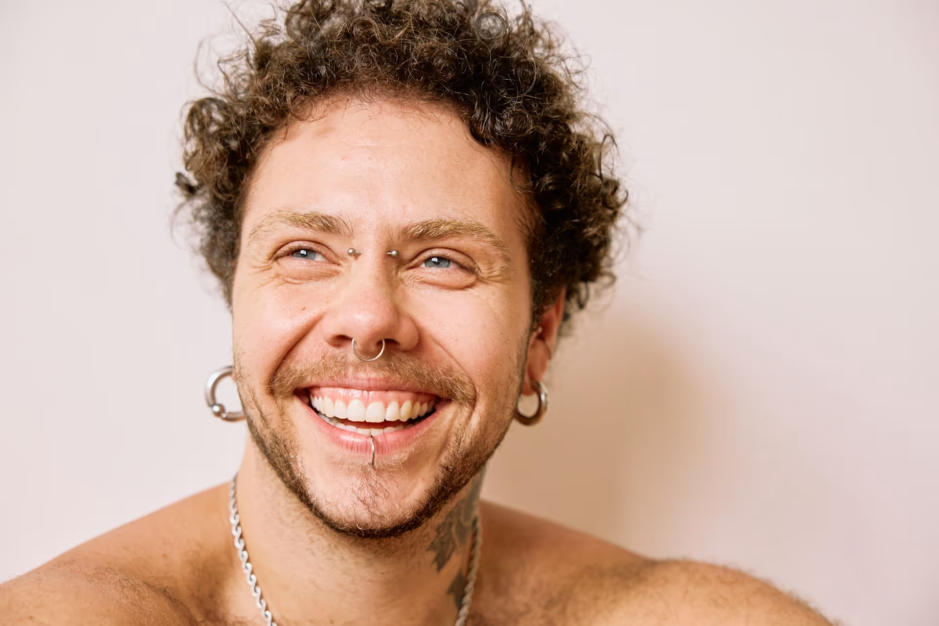 A shirtless man with piercings and a necklace.
