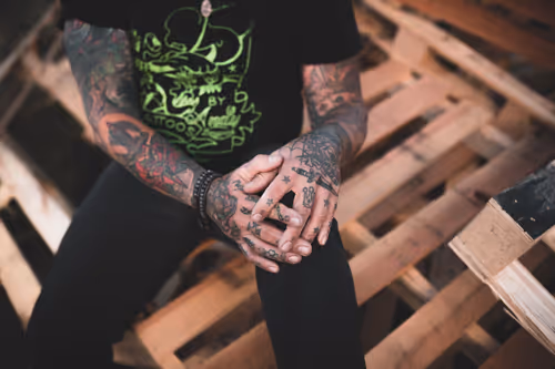 A tattooed man sitting on top of wooden pallets.