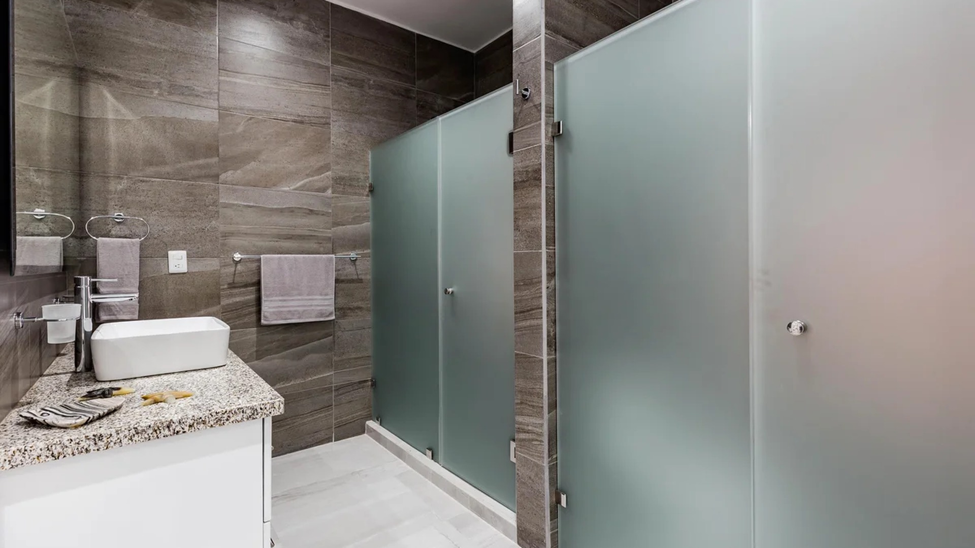 Image of a Modern Bathroom, featuring Frosted Glass Shower Stalls and Stone Tiled Walls.