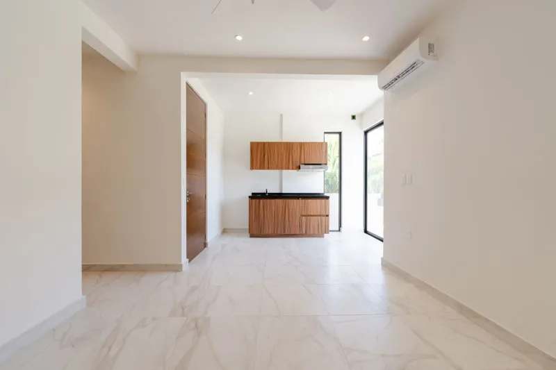 Interior view of a finished luxury unit at Amanecer Condos, featuring a minimalist design with white tiled floors, a modern kitchen area with wooden cabinetry, and an open living space, ready for occupancy.
