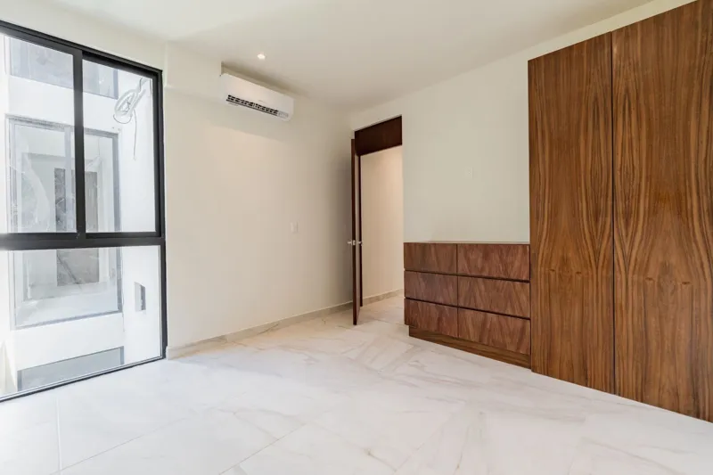 Interior view of a finished luxury unit at Amanecer Condos, featuring a minimalist design with white tiled floors, a modern kitchen area with wooden cabinetry, and an open living space, ready for occupancy.