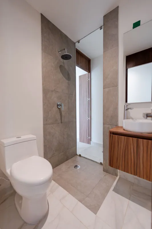 Interior view of a finished luxury unit at Amanecer Condos, featuring a minimalist design with white tiled floors, a modern kitchen area with wooden cabinetry, and an open living space, ready for occupancy.