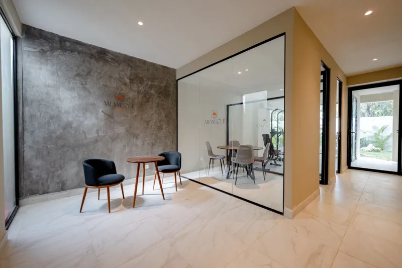 Interior view of a finished luxury unit at Amanecer Condos, featuring a minimalist design with white tiled floors, a modern kitchen area with wooden cabinetry, and an open living space, ready for occupancy.