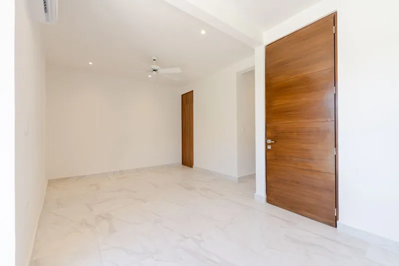 Interior view of a finished luxury unit at Amanecer Condos, featuring a minimalist design with white tiled floors, a modern kitchen area with wooden cabinetry, and an open living space, ready for occupancy.