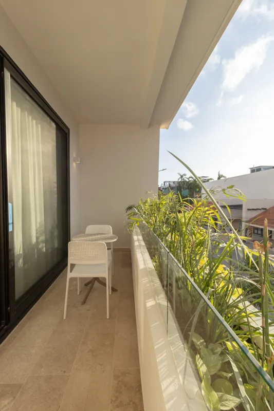 A fully furnished bedroom in a Vibbe model unit, featuring a large bed with a light wood frame, a wall-mounted television, a black ceiling fan, and light-colored walls adorned with decorative woven plates. A built-in light wood closet is visible o...