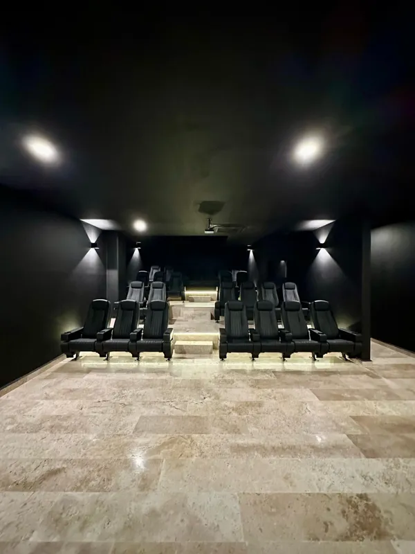 A vibrant rooftop pool bar at TownCenter Zama, featuring a sparkling blue swimming pool, a bar counter with four wooden stools, and modern pendant lights, all set against a clear blue sky with lush green foliage in the background, showcasing a rea...