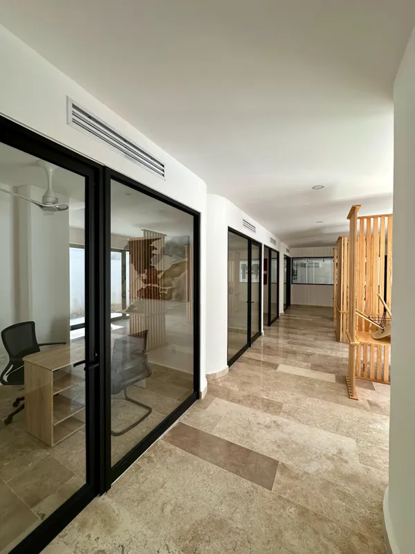 A vibrant rooftop pool bar at TownCenter Zama, featuring a sparkling blue swimming pool, a bar counter with four wooden stools, and modern pendant lights, all set against a clear blue sky with lush green foliage in the background, showcasing a rea...