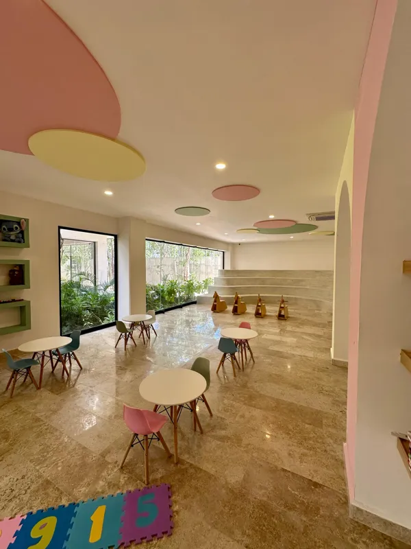 A vibrant rooftop pool bar at TownCenter Zama, featuring a sparkling blue swimming pool, a bar counter with four wooden stools, and modern pendant lights, all set against a clear blue sky with lush green foliage in the background, showcasing a rea...